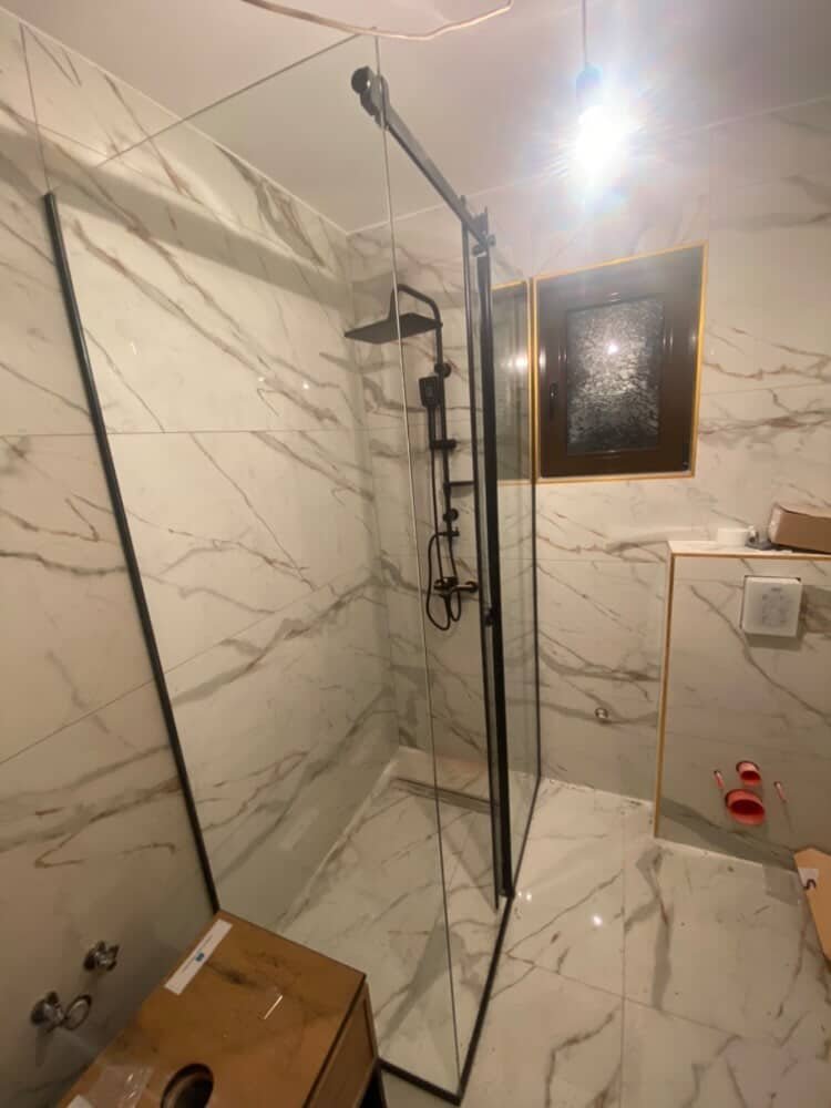 Moderno završeno kupatilo sa mermernim pločicama i staklenom tuš kabinom